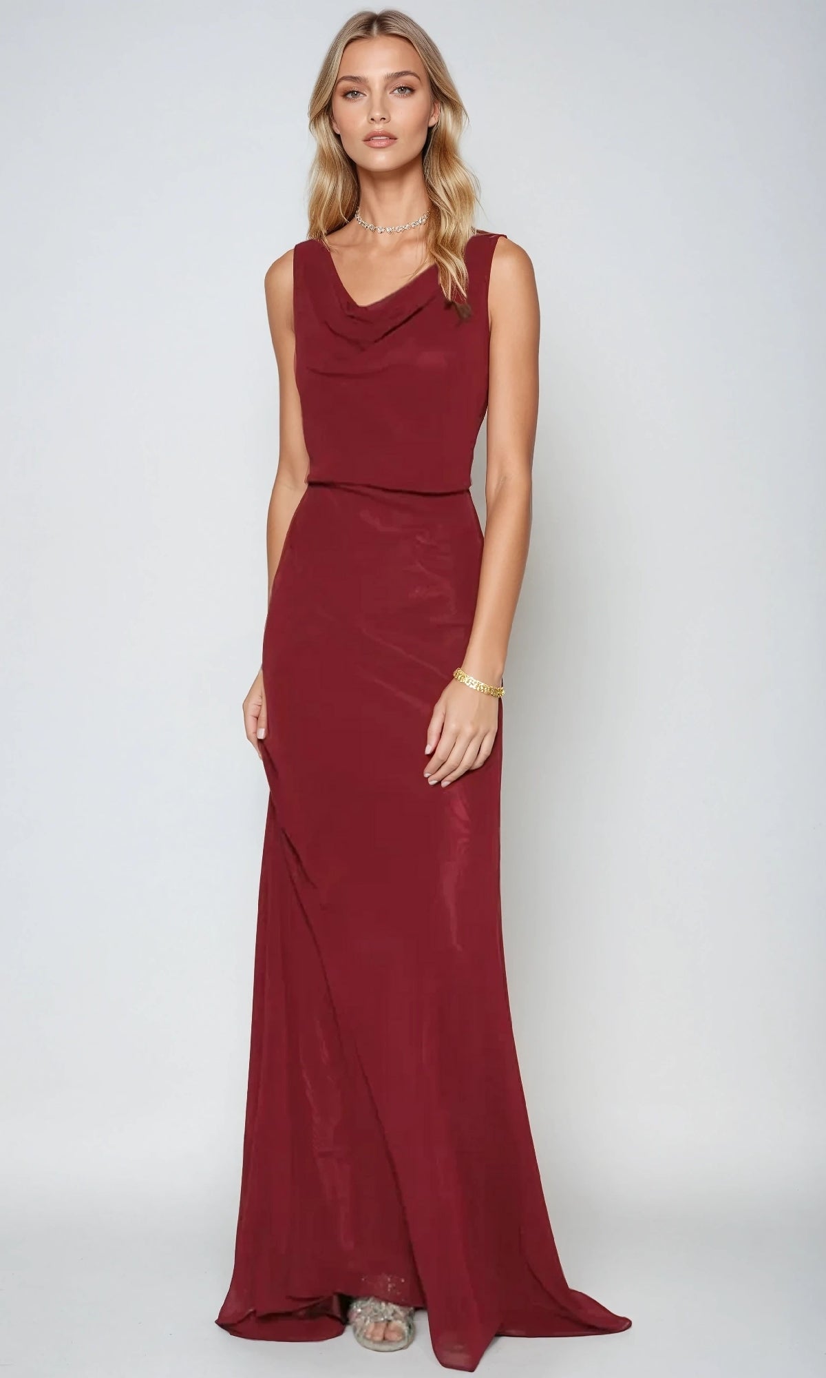 A woman stands against a plain backdrop wearing the Juliet 670, a long burgundy prom dress with a graceful cowl neckline and subtle jewelry.